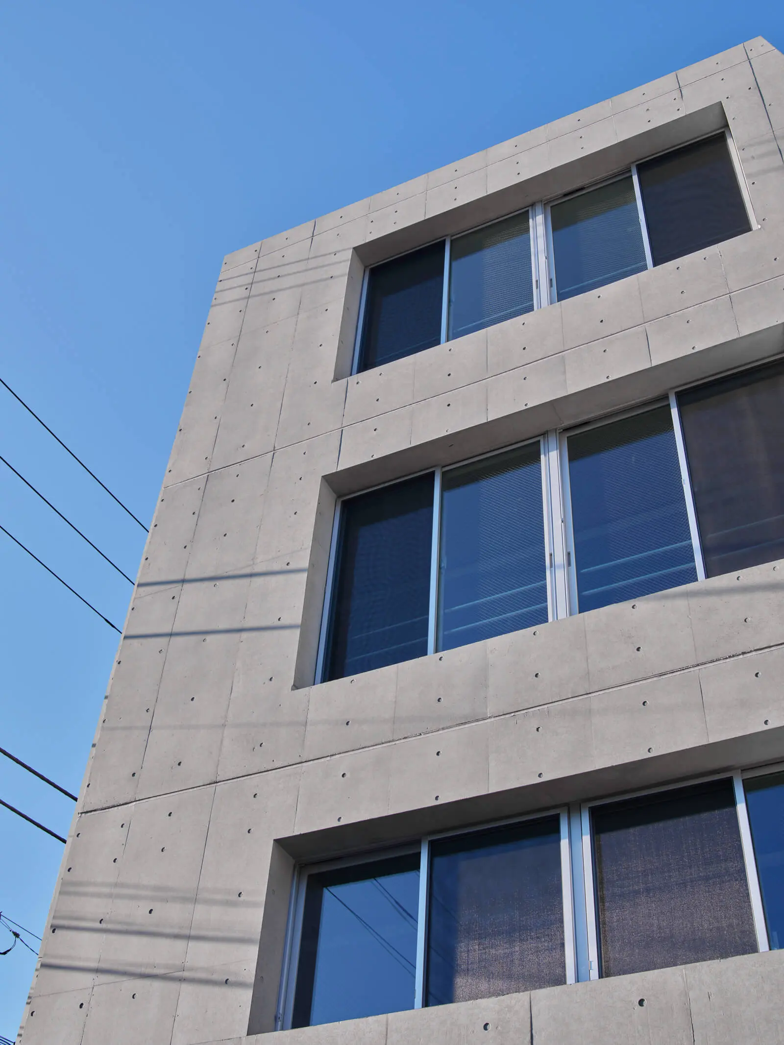 自社ビルのコンクリート打放し外壁と窓のディテール。厚さ300mmの壁に大開口を設け、躯体の軽量化を図っています。