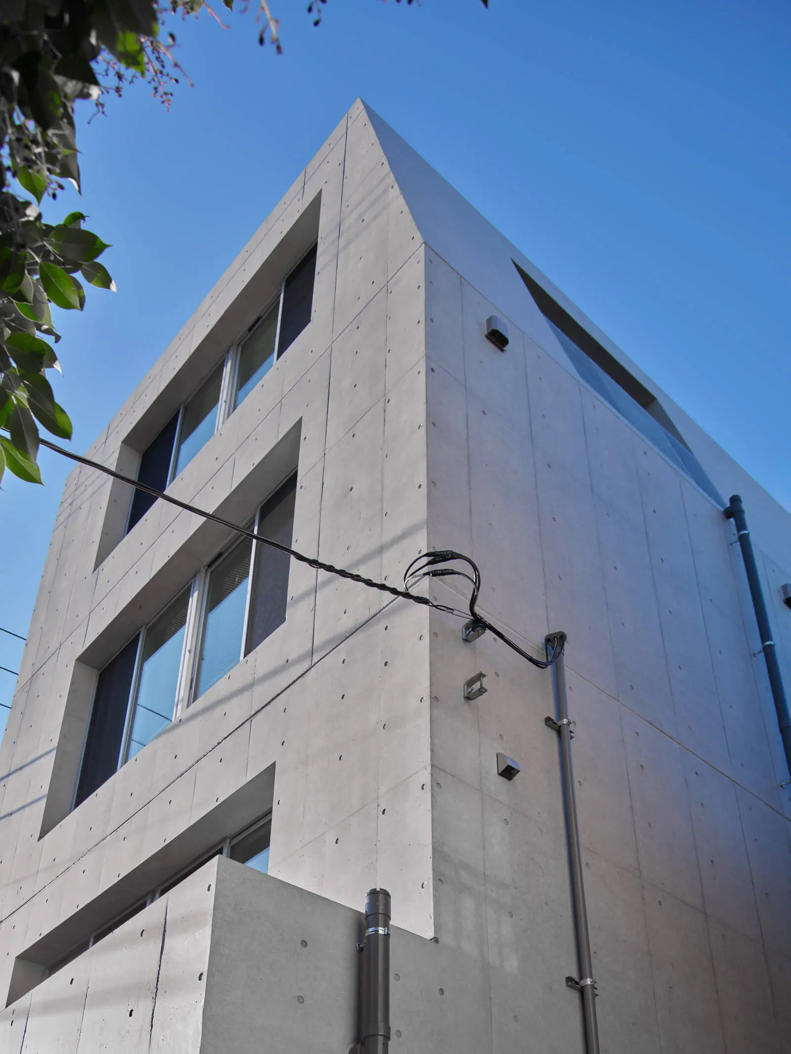 高度斜線制限に対応したオフィスの斜壁デザイン。打放し仕上げで統一し、設備手摺もフラットに納めた美しい北側外観です。