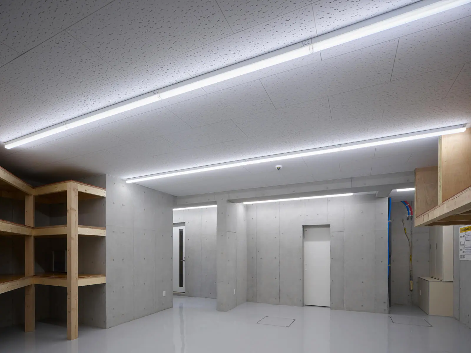 RC造オフィスビル1階の倉庫空間。無機質なコンクリート壁と頑丈な造作木製作業棚の対比が美しい内装デザインです。