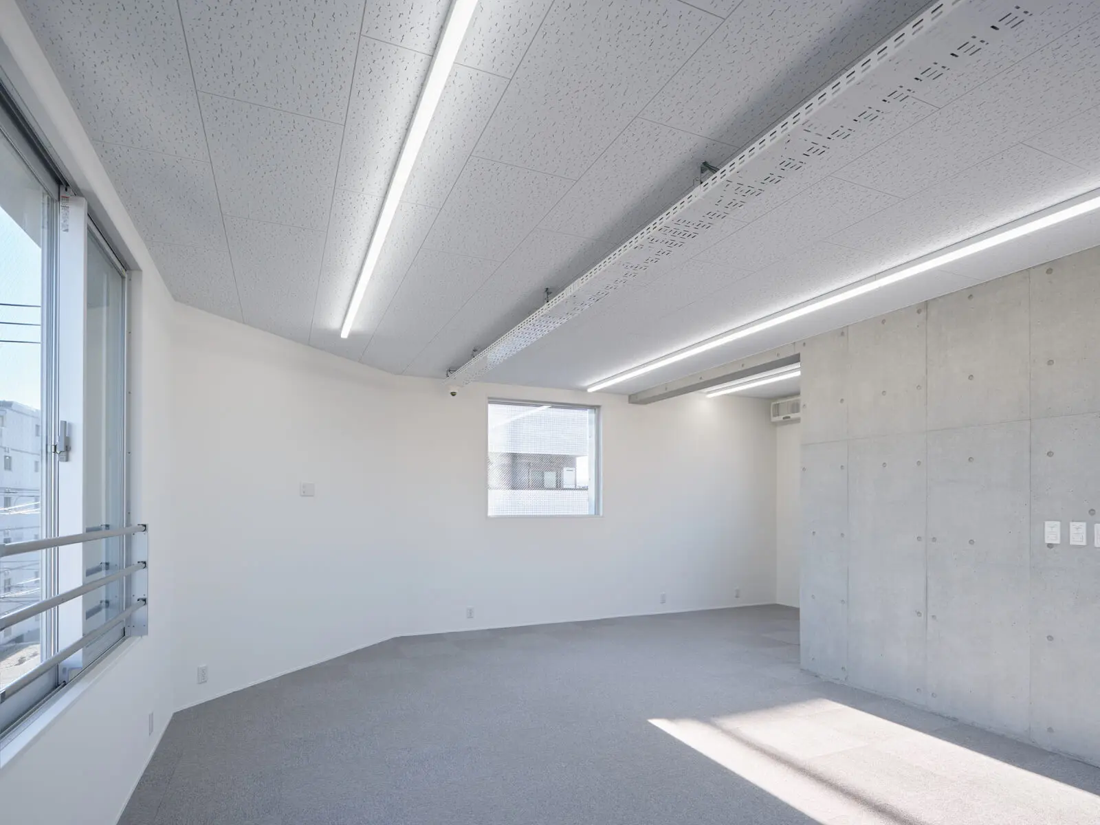 コストダウンと快適性を両立したオフィスビル4階会議室。断熱材を施した白い壁とコンクリート打放し壁の対比。