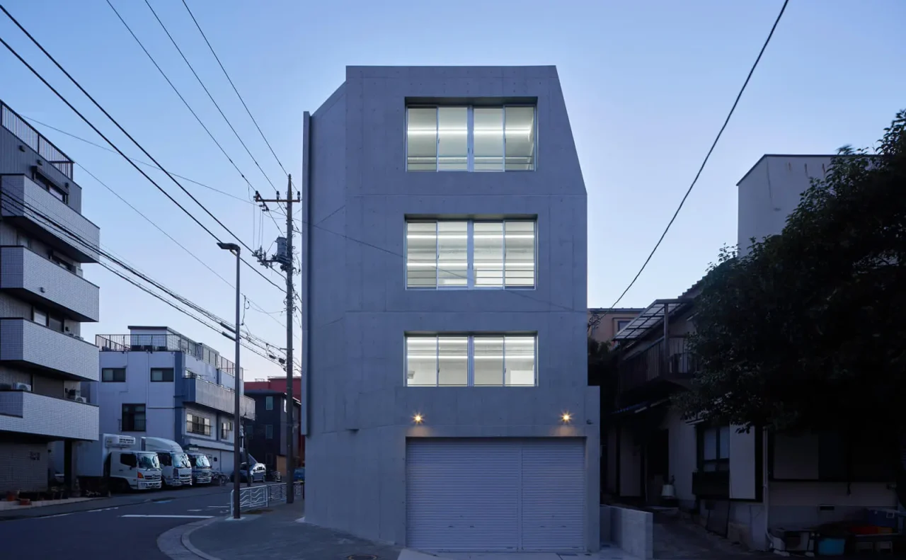 大開口窓から室内の光が溢れるRC造オフィスビルの東側正面外観（夕景）。コストダウンとデザイン性を両立。