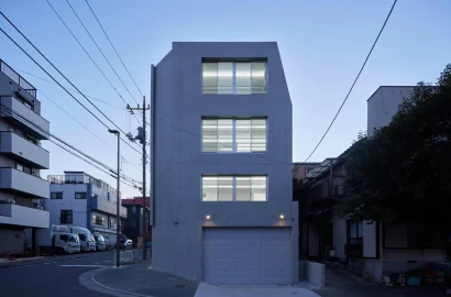 大開口窓から室内の光が溢れるRC造オフィスビルの東側正面外観（夕景）。コストダウンとデザイン性を両立。