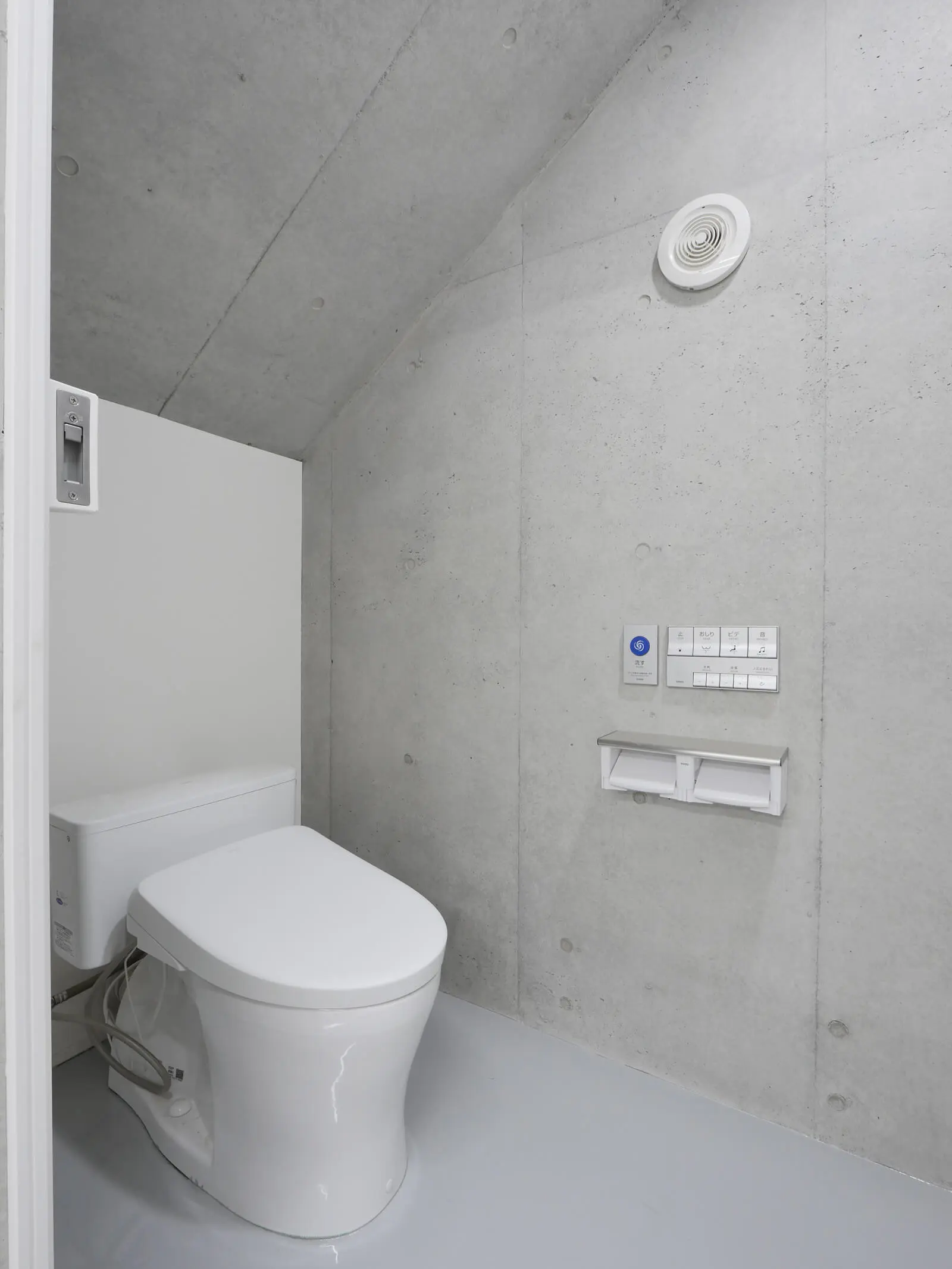 無骨なコンクリート壁が際立つ、RC造4階建て自社ビルの1階階段下トイレ（別アングル）。