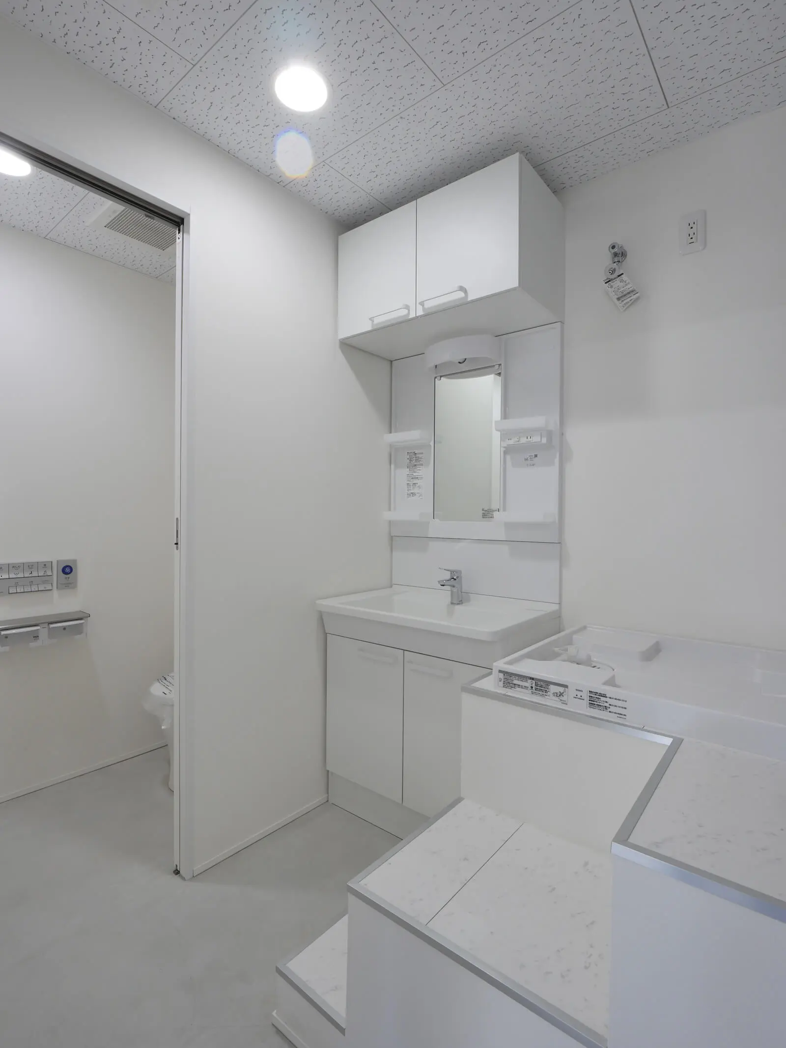 階段上部の余剰空間を洗濯機パンの設置に有効活用した、RC造オフィスビル2階の洗面・洗濯室。