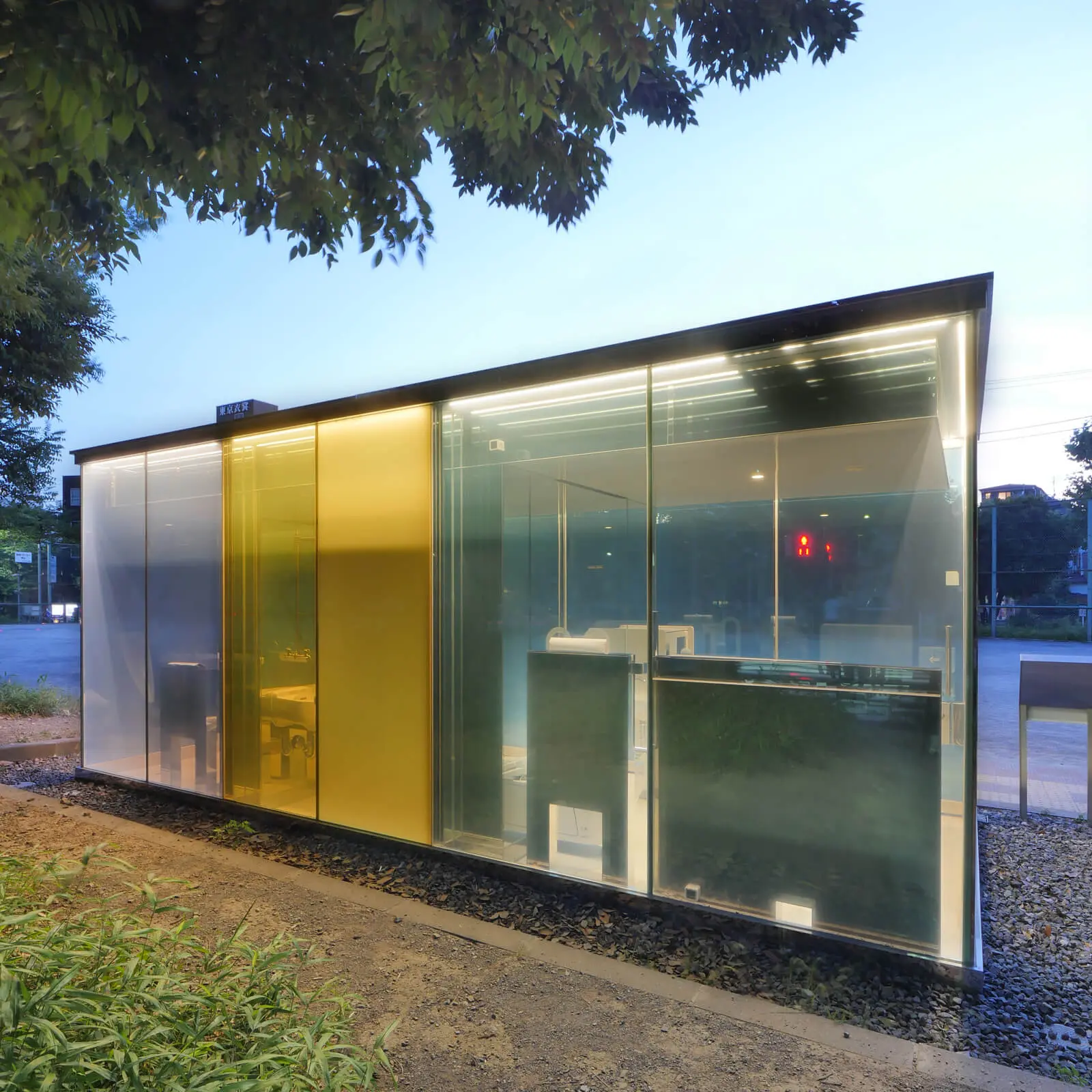 建築家・坂茂が設計したTHE TOKYO TOILET（代々木深町小公園・はるのおがわコミュニティパーク）の透明トイレ外観背面。通電フィルムを用いたガラス張りの建築。