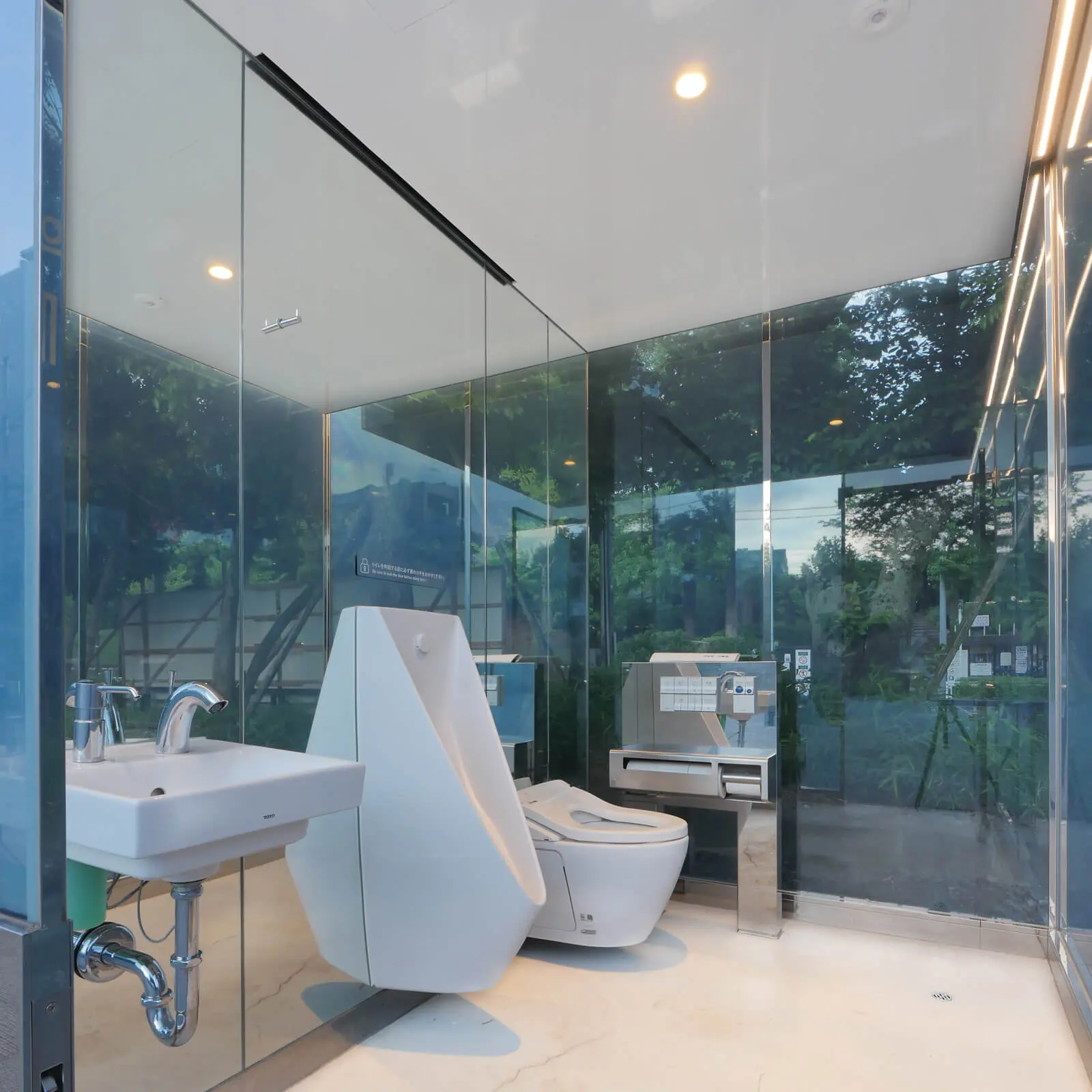 THE TOKYO TOILETプロジェクト・坂茂設計の男子トイレ内部。施錠前は外の景色が透けて見え、TOTO製衛生機器が設置された清潔な空間。