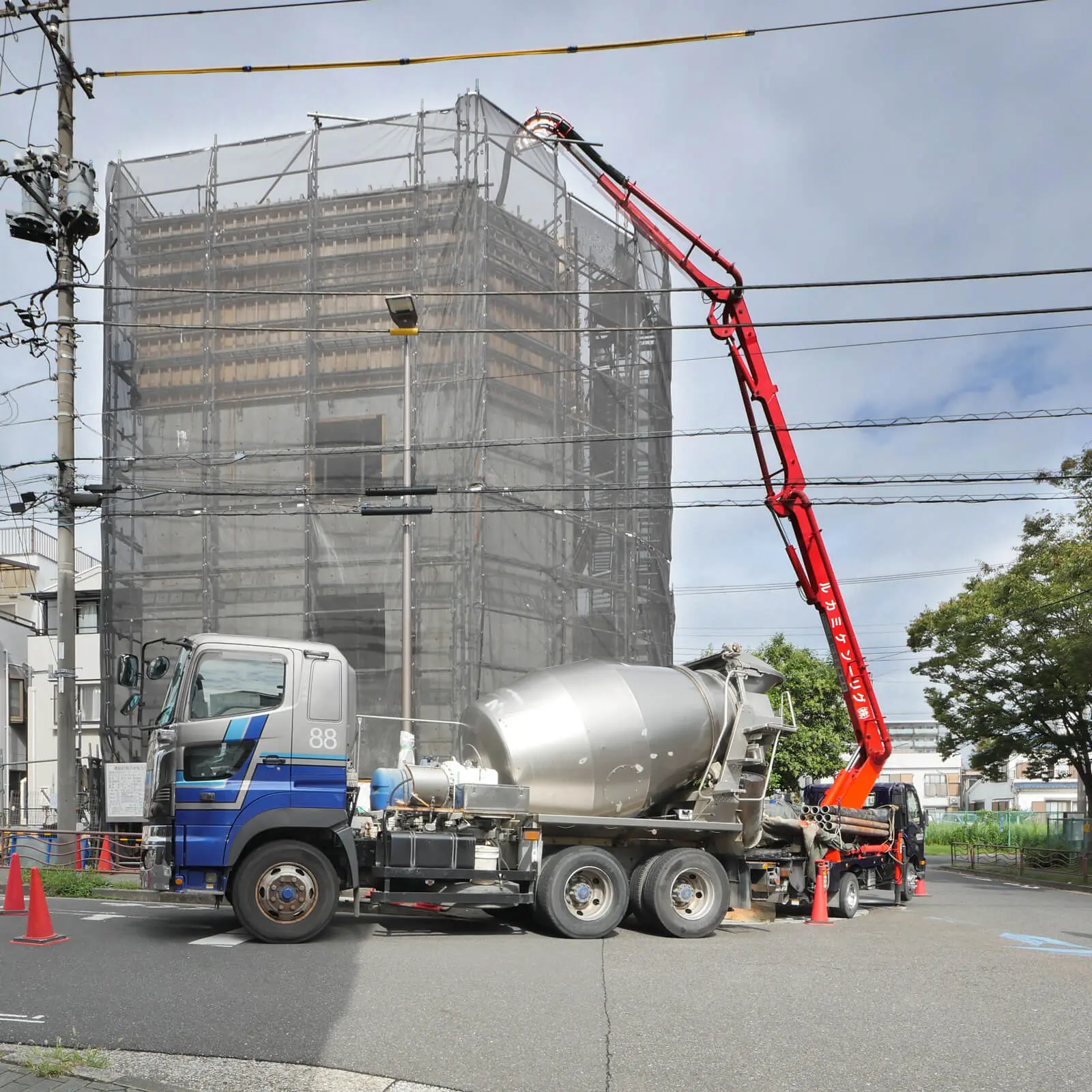 上棟日、屋上階コンクリート打設中の南側外観。ミキサー車とポンプ車が横付けされ、コンクリートを圧送している(江東区潮見 RC造4階建てコンクリート打放しオフィスビル)