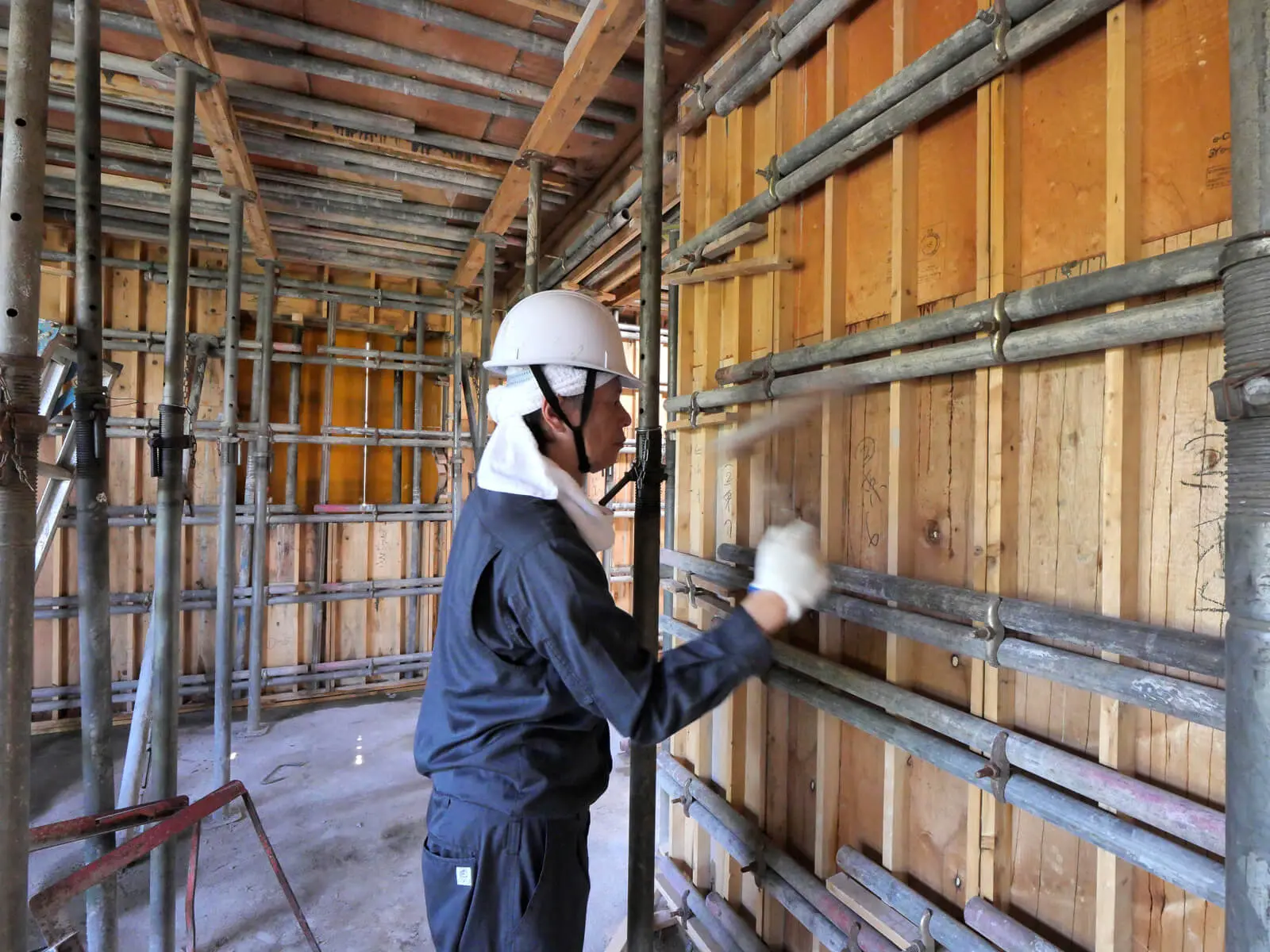 東京都江東区で建設中の鉄筋コンクリート造オフィスビル。3階事務室で設計監理者の片岡が打設中のコンクリート打放し仕上げの型枠を木槌で叩き、密実なコンクリートとなるよう品質管理を行っている様子。