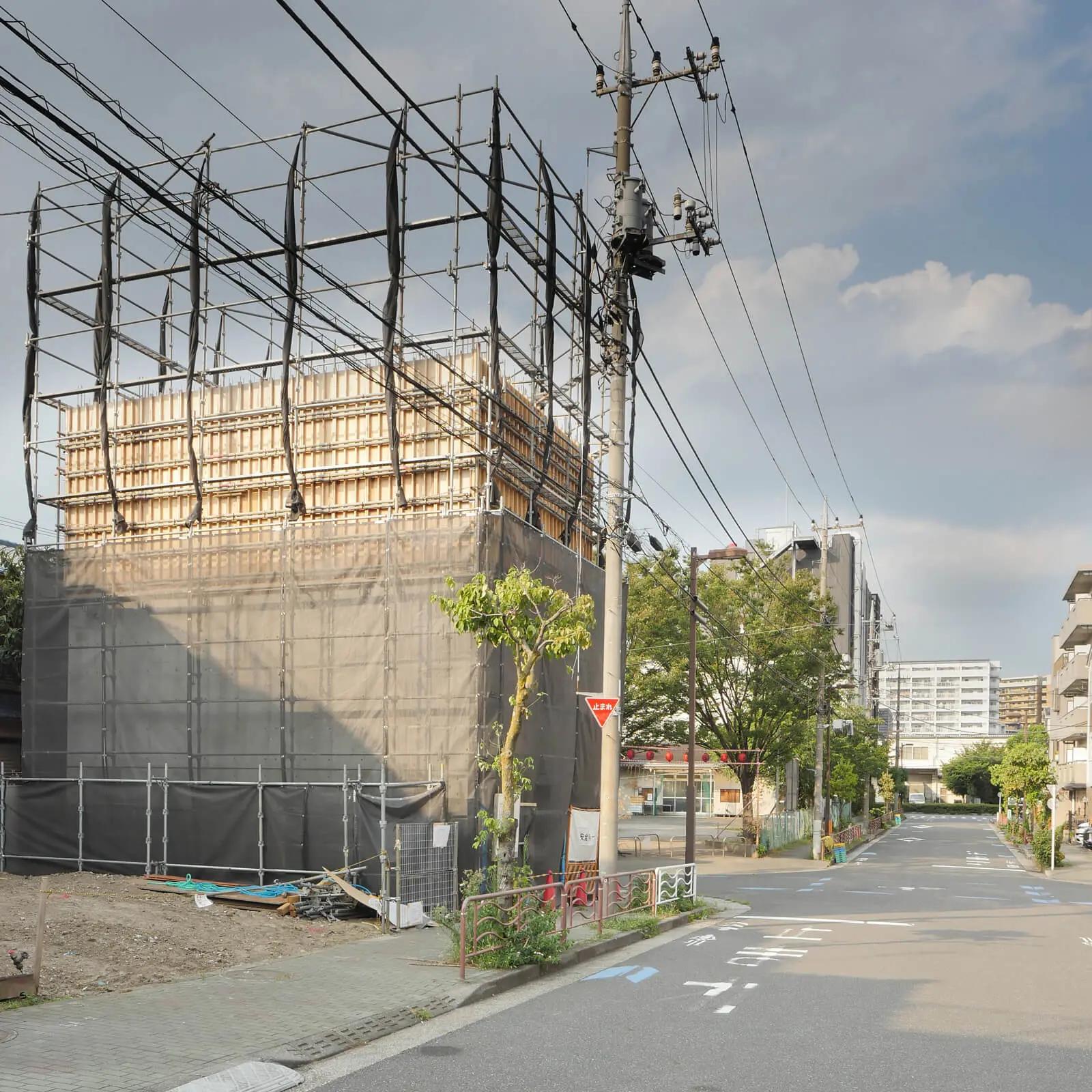 江東区潮見のRCオフィスビル西側外観。街並みの中で3階型枠工事が進む鉄筋コンクリート造オフィスビル道向かいの公園では夏祭りの提灯が飾られています。
