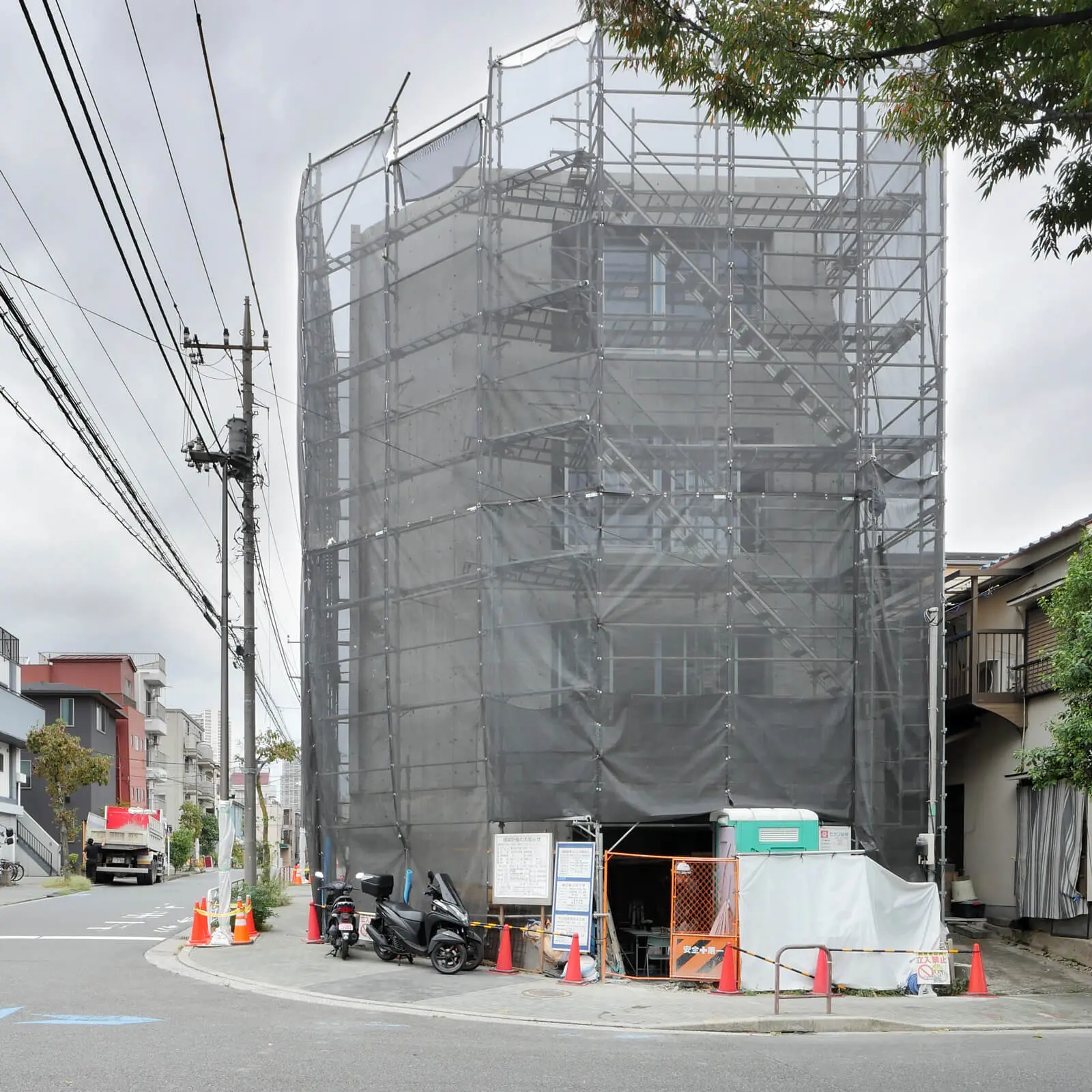 サッシとガラスの取付けが完了した東側外観。足場と養生シートに覆われたRC造4階建てオフィスビル(江東区潮見)